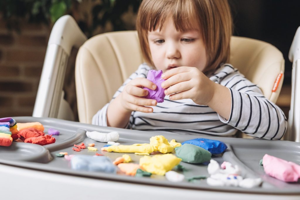 Cute little boy molding with colorful plasticine on table at home. Development of fine motor skills.