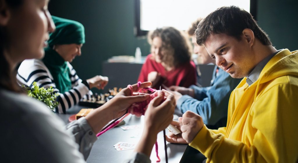 Group of people playing cards and board games in community center, inclusivity of disabled person